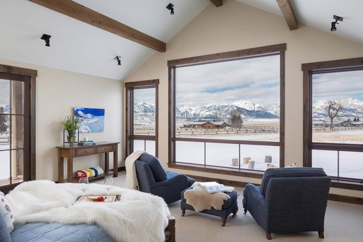 Bedroom with vaulted ceiling, blue armchairs, and large windows overlooking snowy mountain view