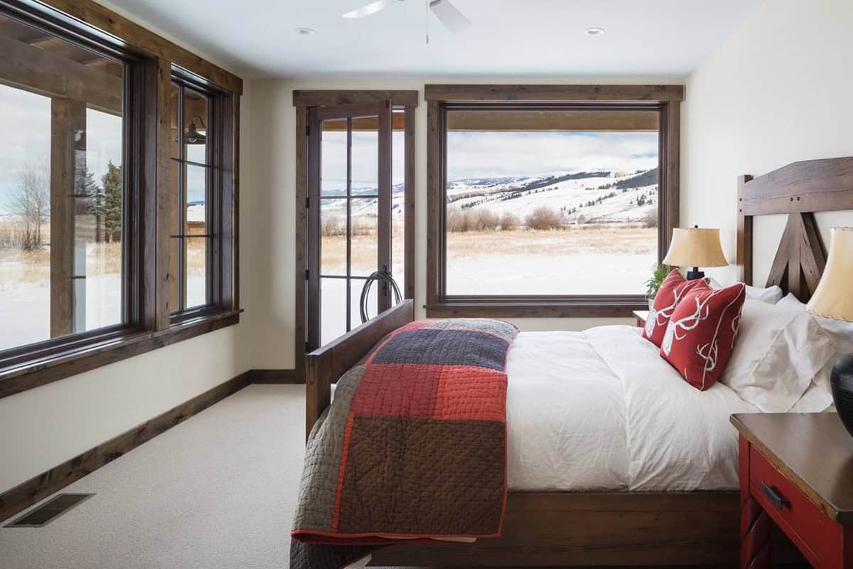 Bedroom with wood-framed bed, red patchwork quilt, and large window showing snowy landscape