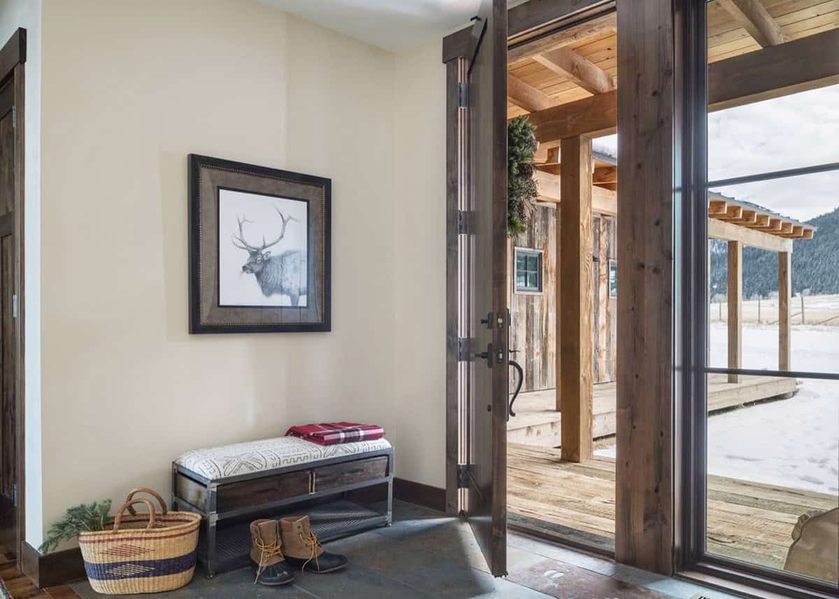 Entryway with elk artwork, storage bench, boots, and open door showing porch and mountains