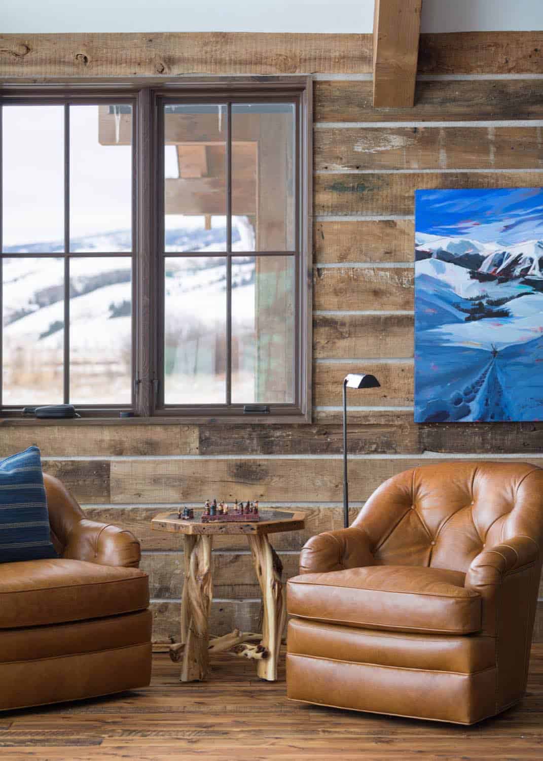 Reading nook with two tan leather chairs, wood side table, and mountain landscape painting