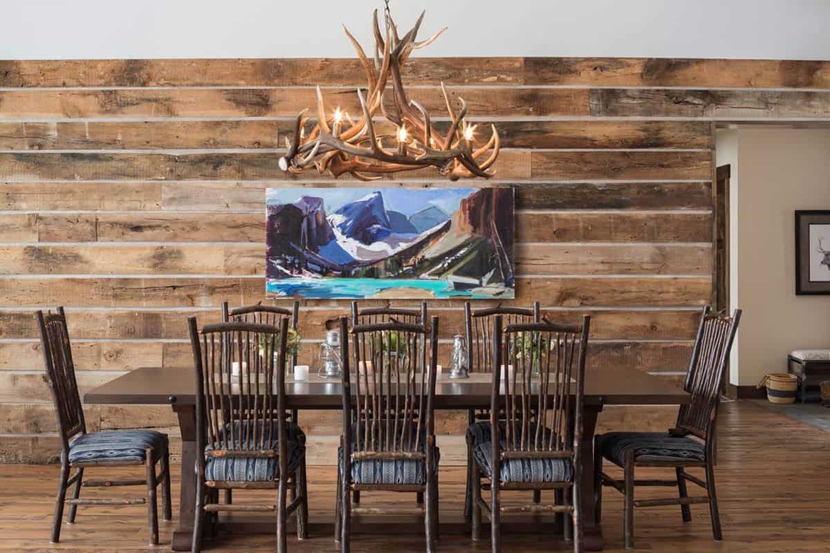 Dining room with wooden table, antler chandelier, mountain painting, and rustic hickory chairs