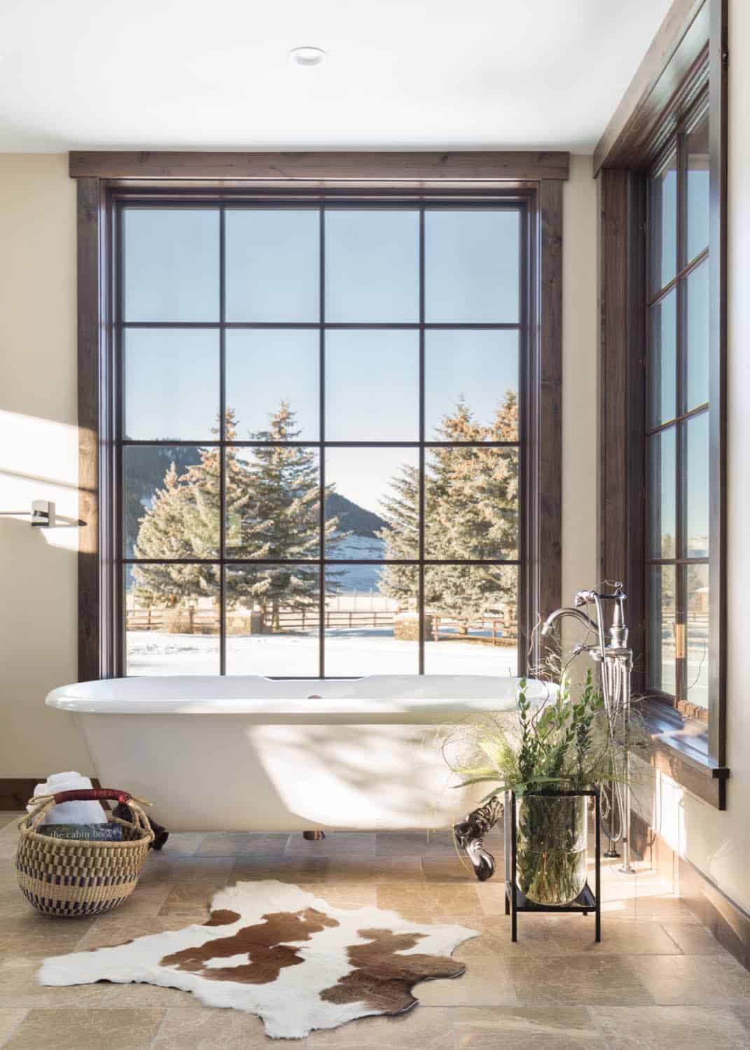 Bathroom with clawfoot tub, cowhide rug, and large window overlooking snowy pine trees