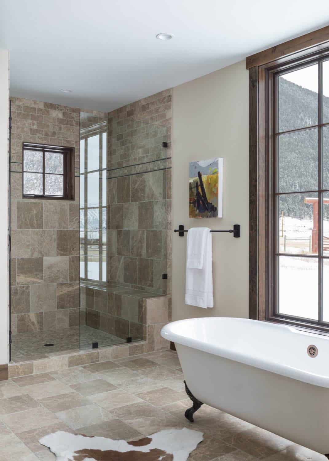 Bathroom with clawfoot tub, tiled walk-in shower, and window overlooking snowy hillside