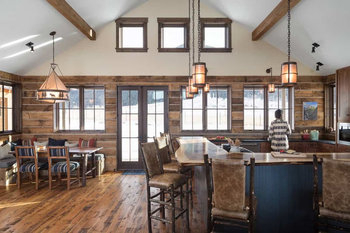 Open kitchen and dining area with high ceilings, wood beams, and banquette seating by windows