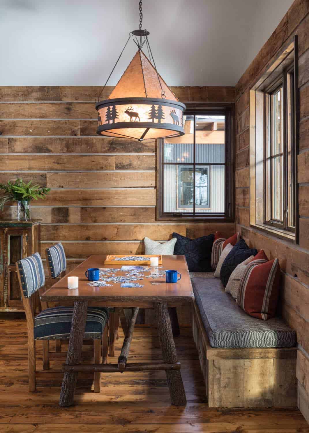 Cozy dining nook with rustic elk-motif pendant light, striped chairs, and puzzle on wood table