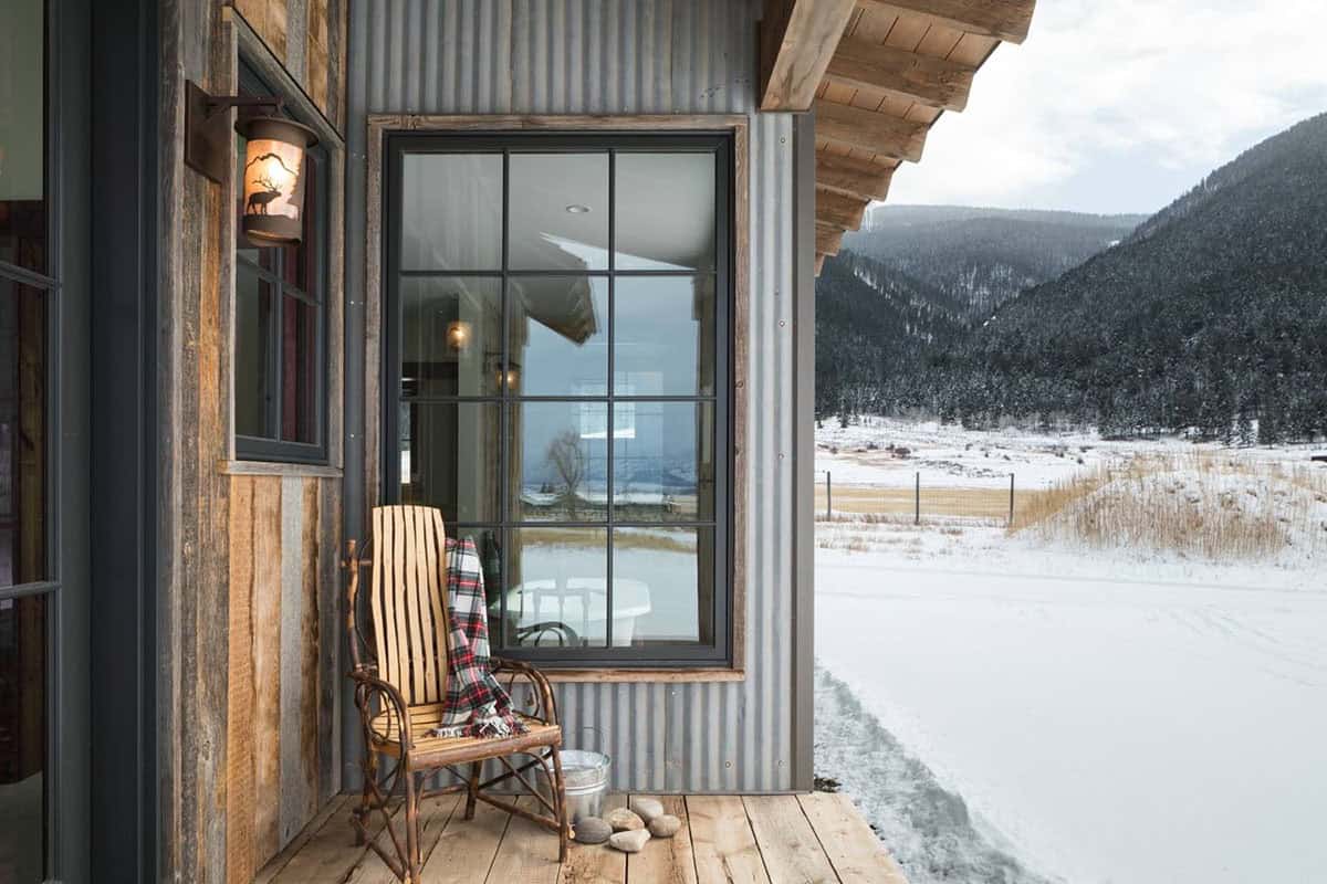 Covered porch corner with wooden rocking chair, plaid throw, and snowy mountain valley view