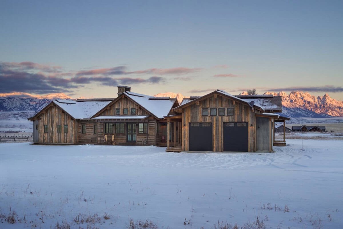 Wood-sided home with attached garage at sunrise, snowy field and Teton mountains in background