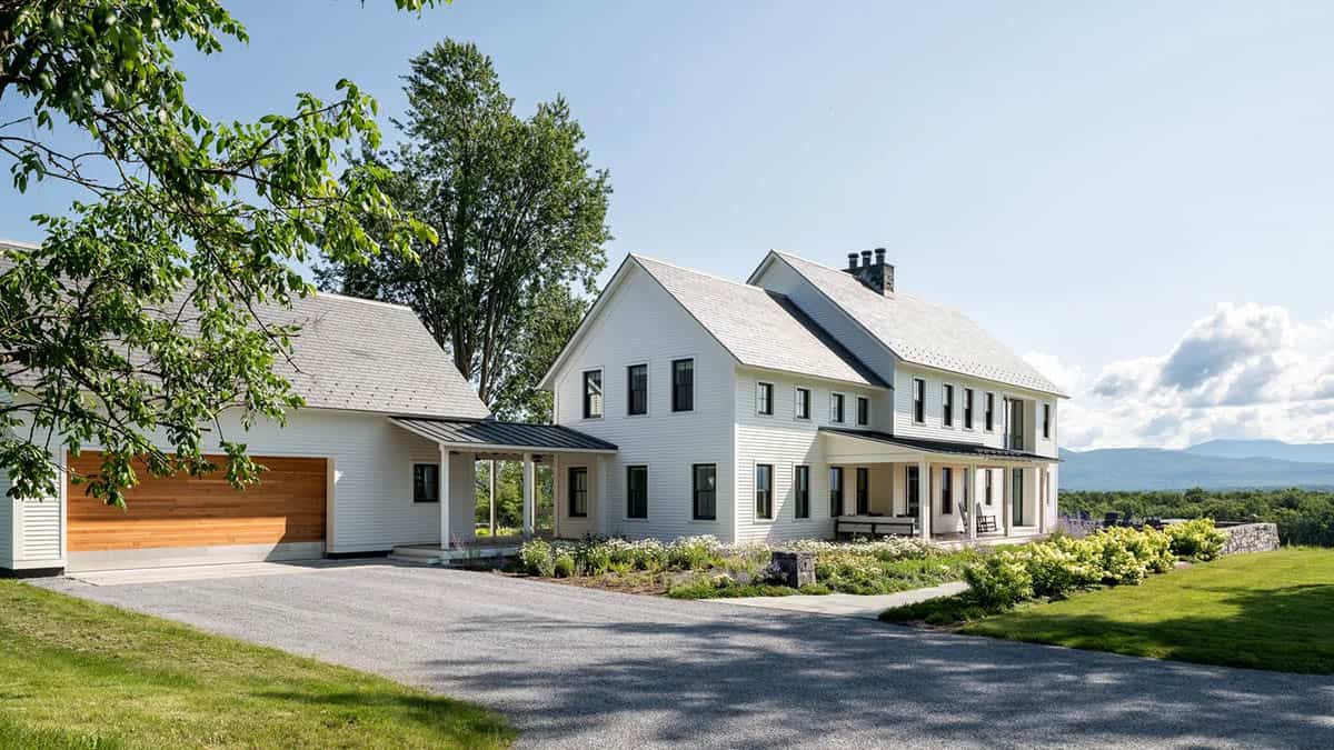 White modern farmhouse in Cornwall, Vermont with slate roof, cedar garage door, and gravel drive
