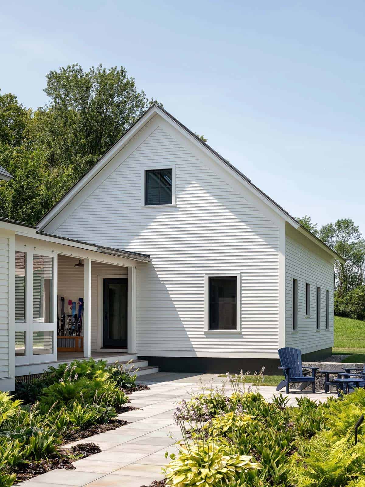 Gabled farmhouse wing with white clapboard siding, bluestone patio, and blue Adirondack chairs