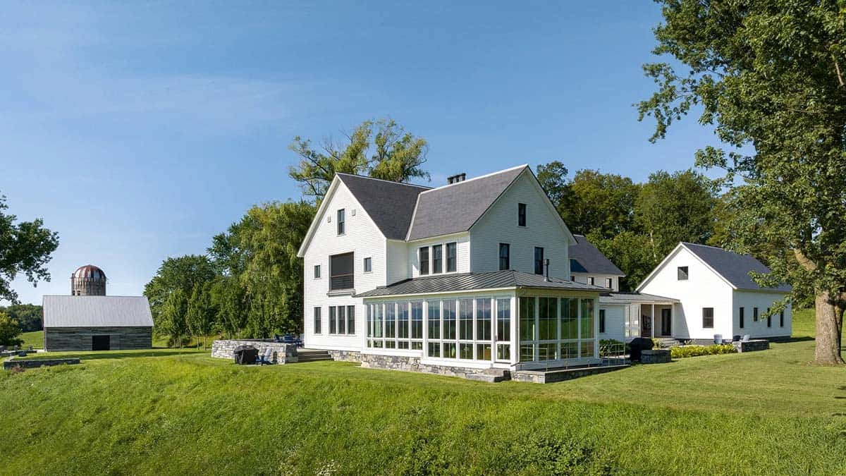 Rear of the Vermont farmhouse with sunroom, stone terrace, and barn with silo beyond