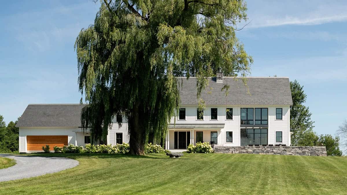 Farmhouse front facade behind a weeping willow with cedar garage door and stone wall