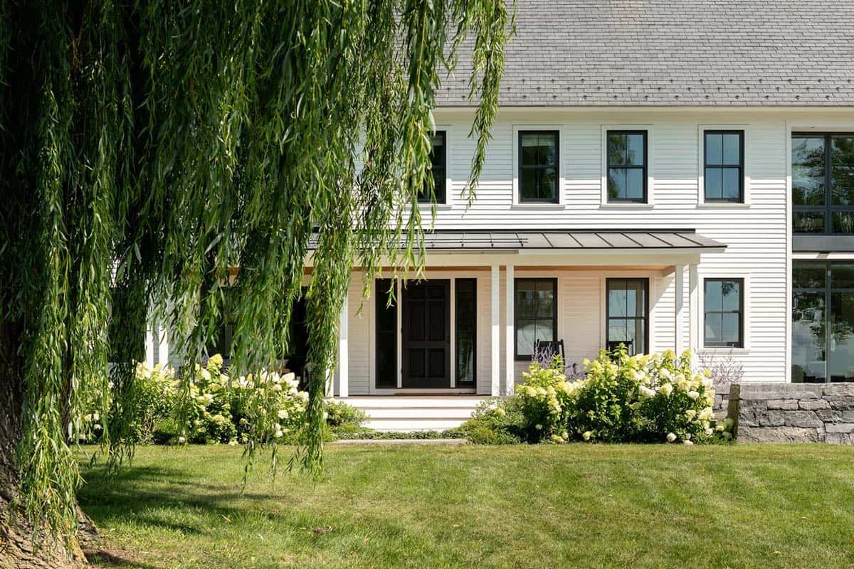 Front porch with black door, standing seam roof, and blooming hydrangeas under willow branches