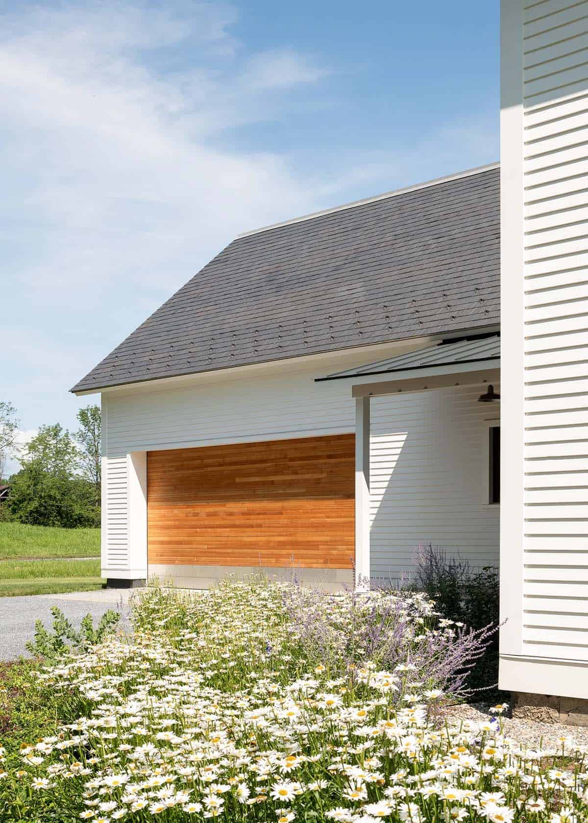 Cedar garage door beneath a slate roof with white daisies in the foreground