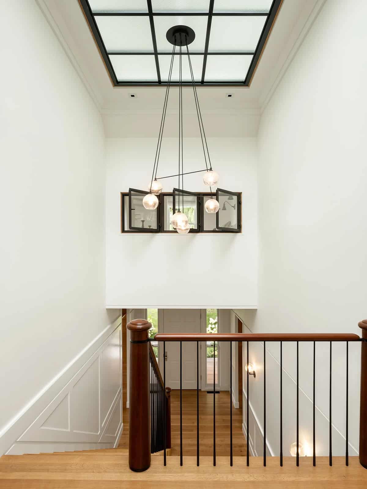Stairwell with steel-framed skylight, pendant chandelier, and interior industrial windows