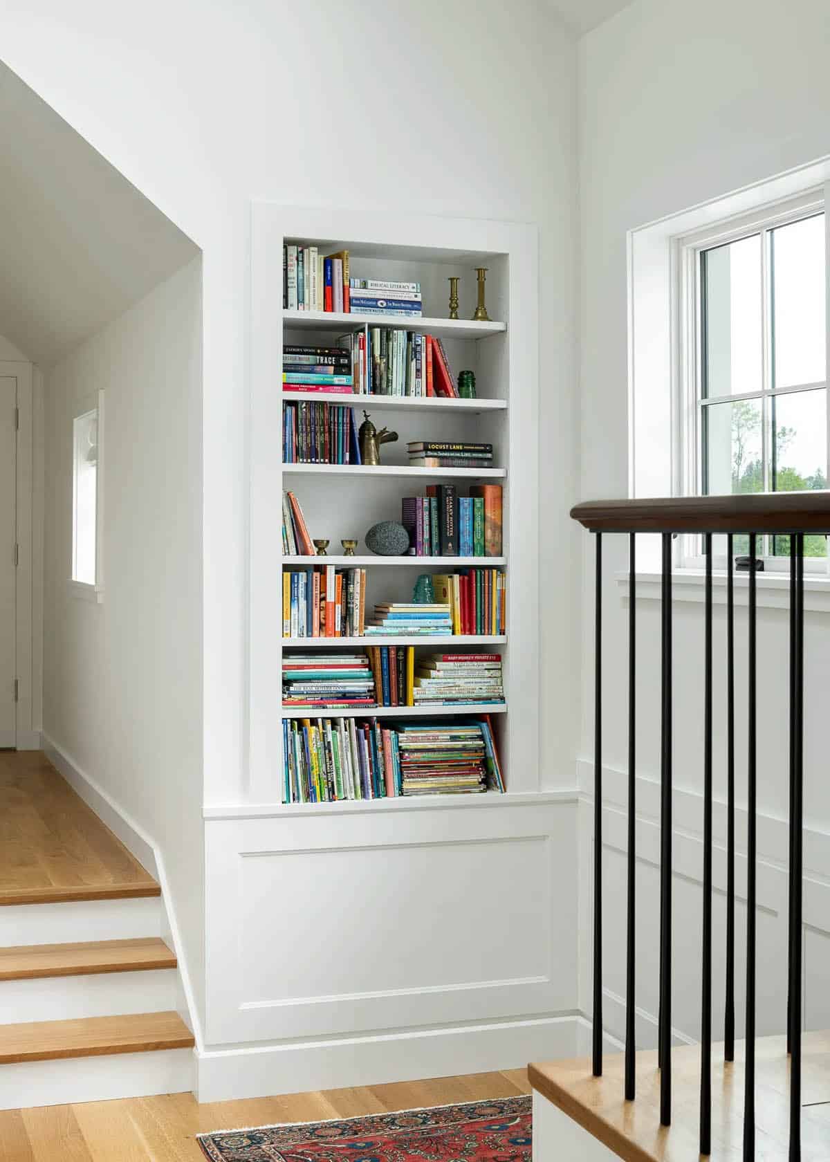 Built-in bookshelf with paneled base beside a stair landing window