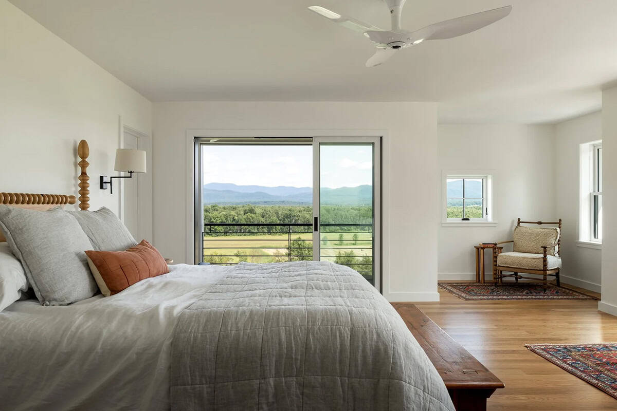 Primary bedroom with spindle bed, linen bedding, and sliding glass door framing mountain views
