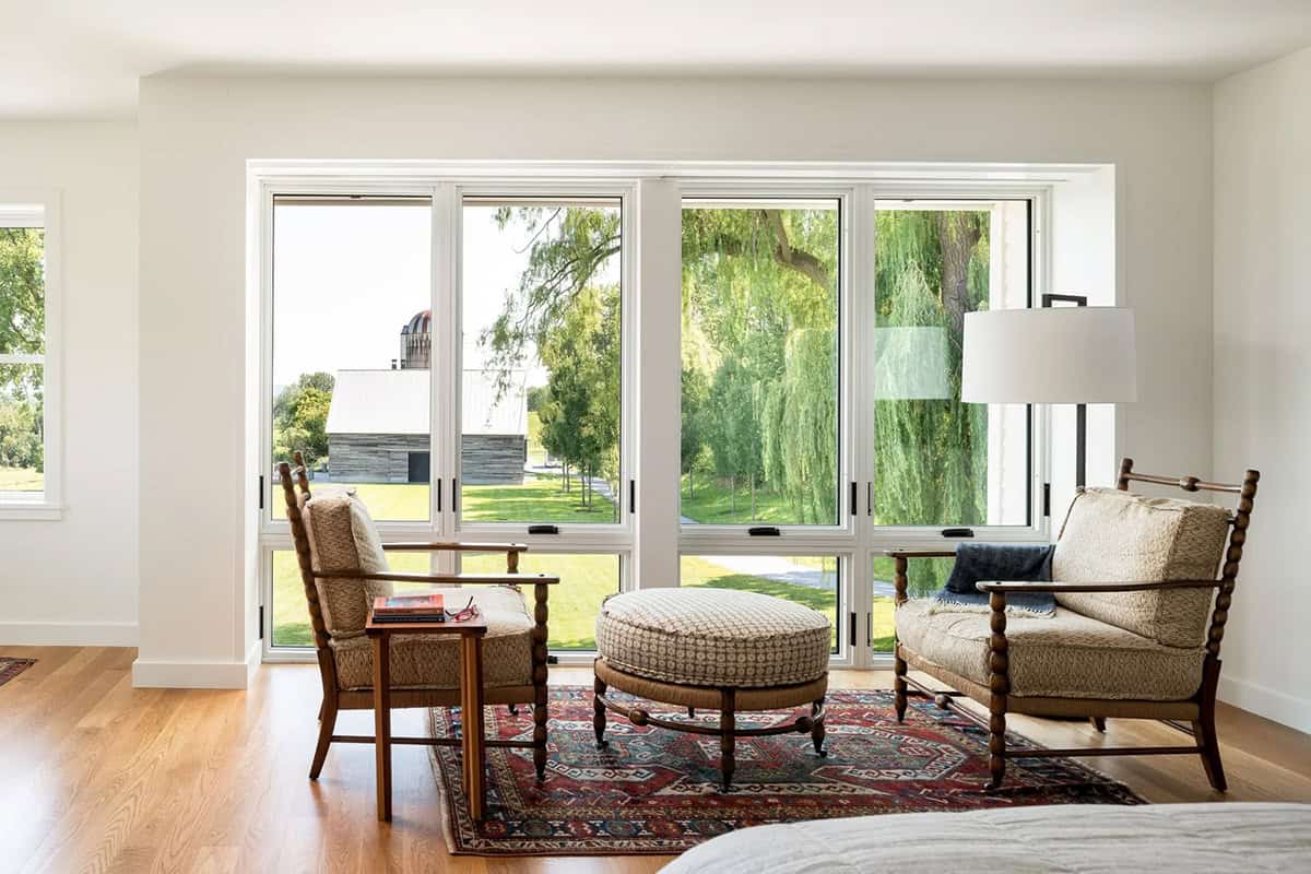 Primary bedroom sitting area with spindle chairs and ottoman overlooking a weeping willow and barn