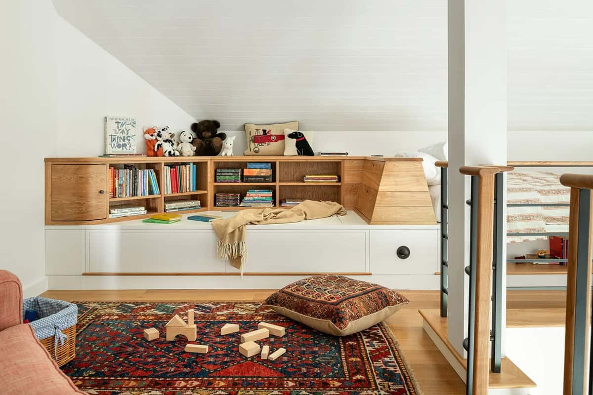 Loft play nook with built-in wood bookshelves, storage bench, and vintage rug