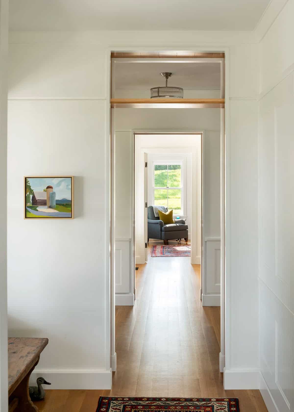 Hallway with paneled walls and oak floors leading through doorways to a sunny sitting room