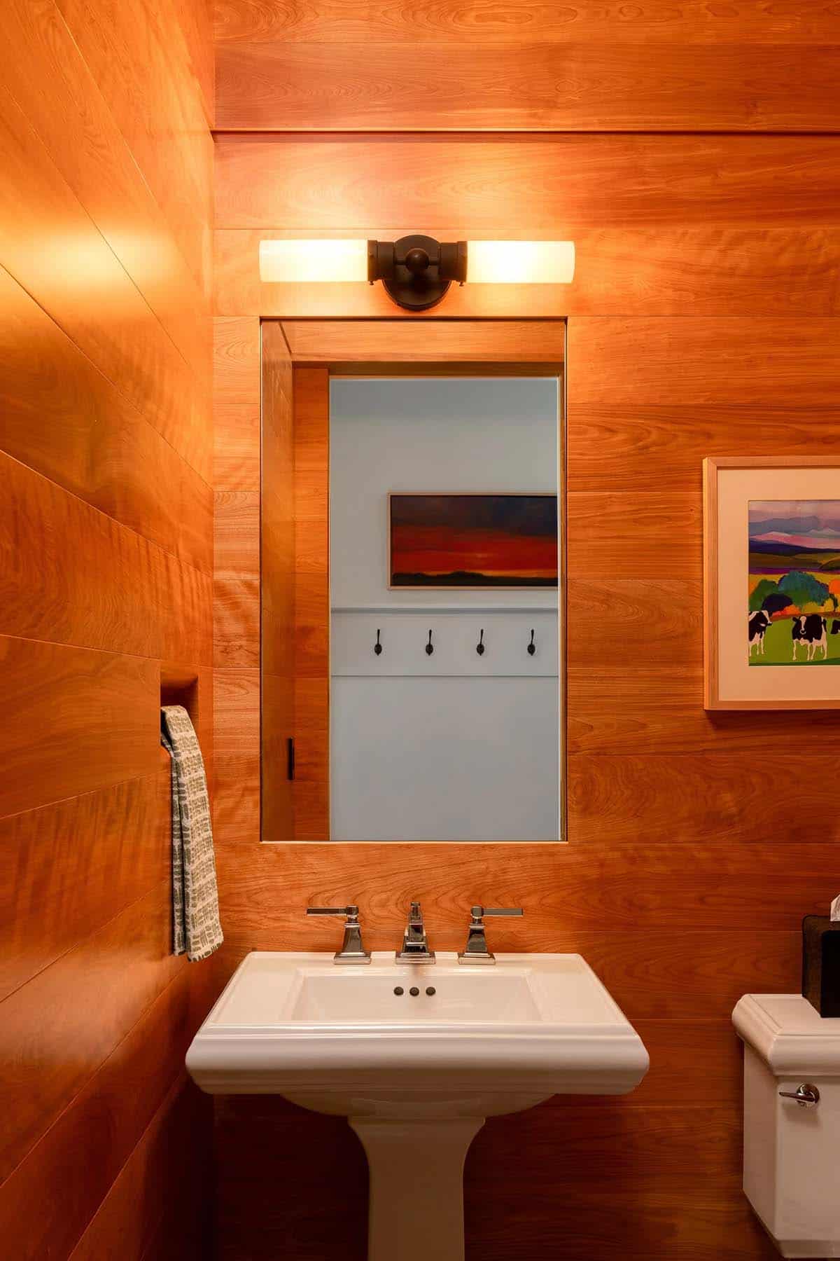 Powder room with wood-paneled walls, pedestal sink, and framed mirror