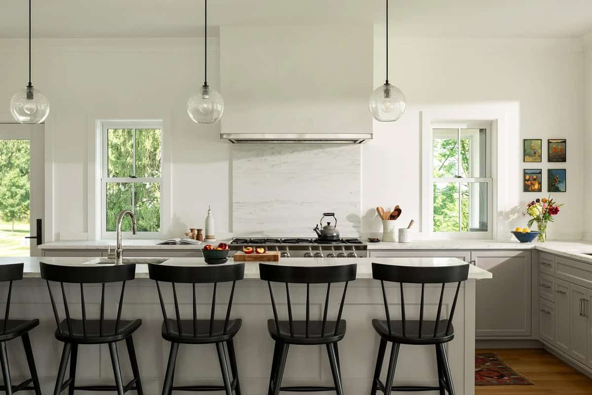 Farmhouse kitchen with marble backsplash, white range hood, and black Windsor counter stools