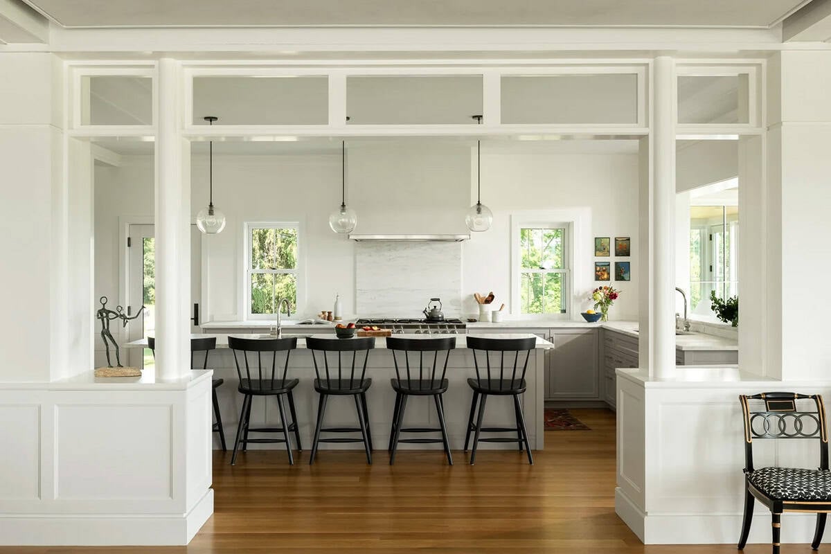 Open kitchen framed by white columns and transom windows, with black stools at the island
