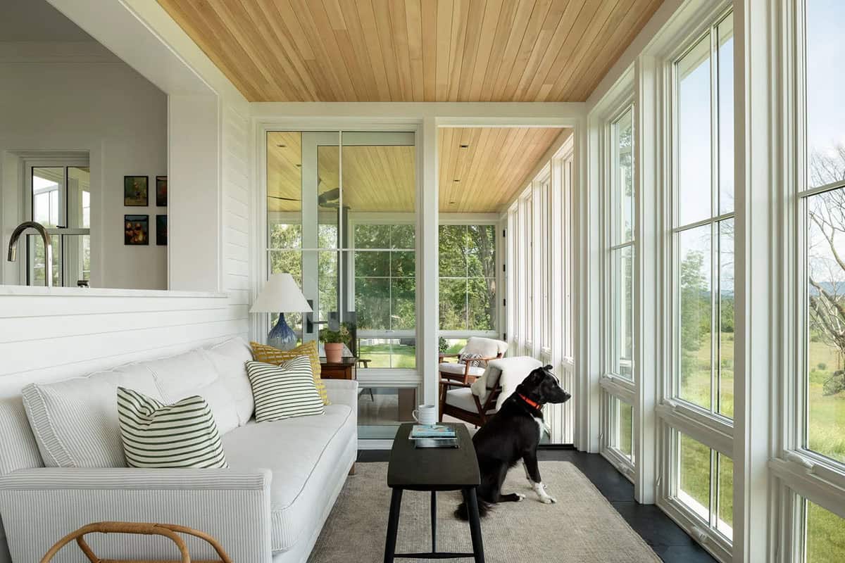 Sunroom with striped sofa, cedar ceiling, and floor-to-ceiling windows facing the meadow