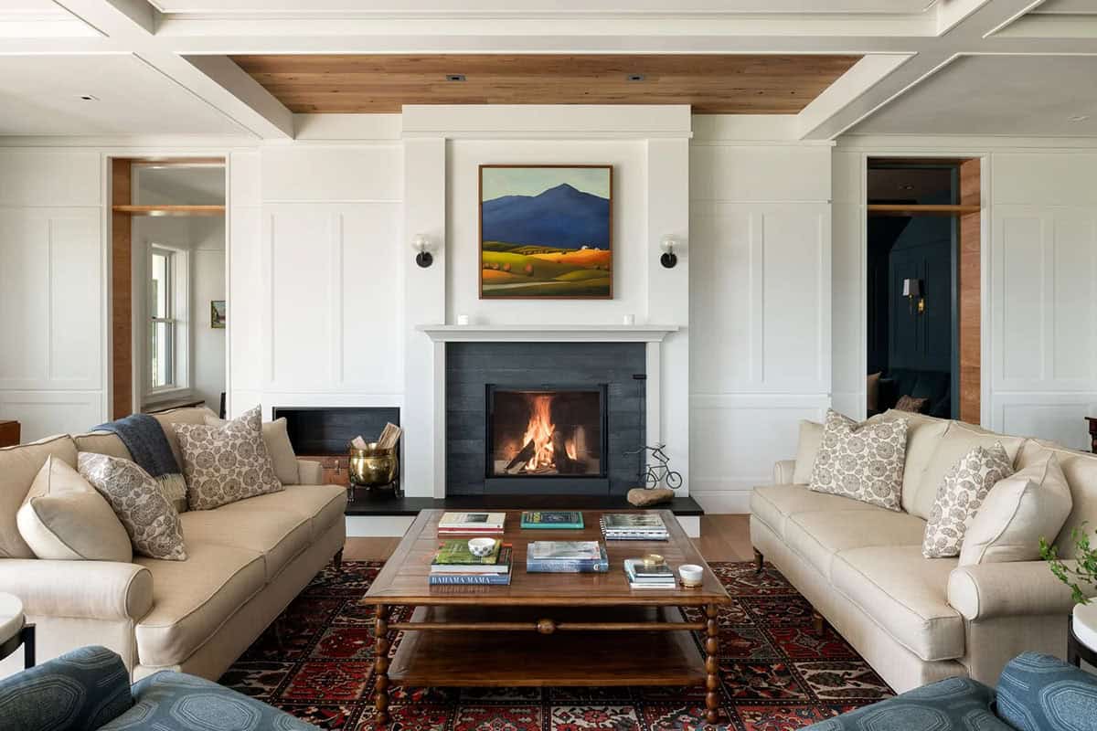 Living room fireplace with dark surround, paneled walls, cream sofas, and reclaimed wood ceiling inset