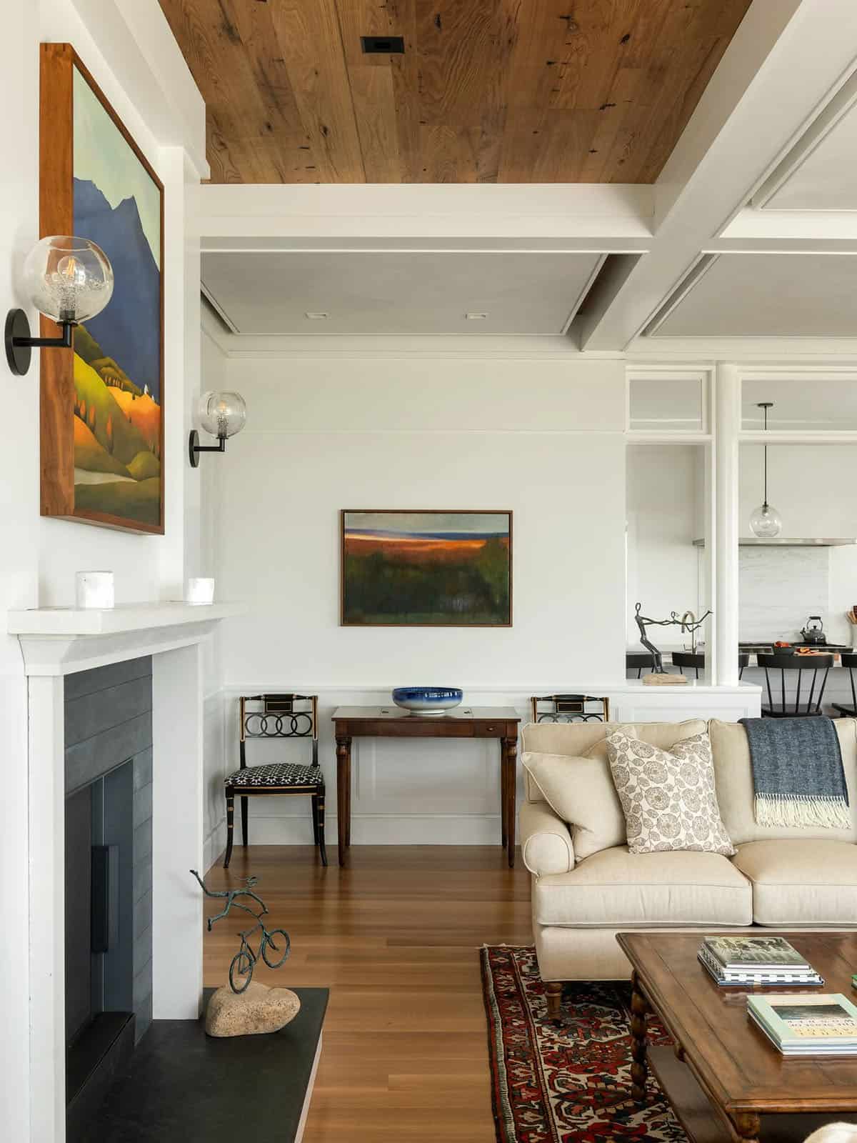 Living room corner with glass globe sconces, landscape paintings, and a view into the kitchen