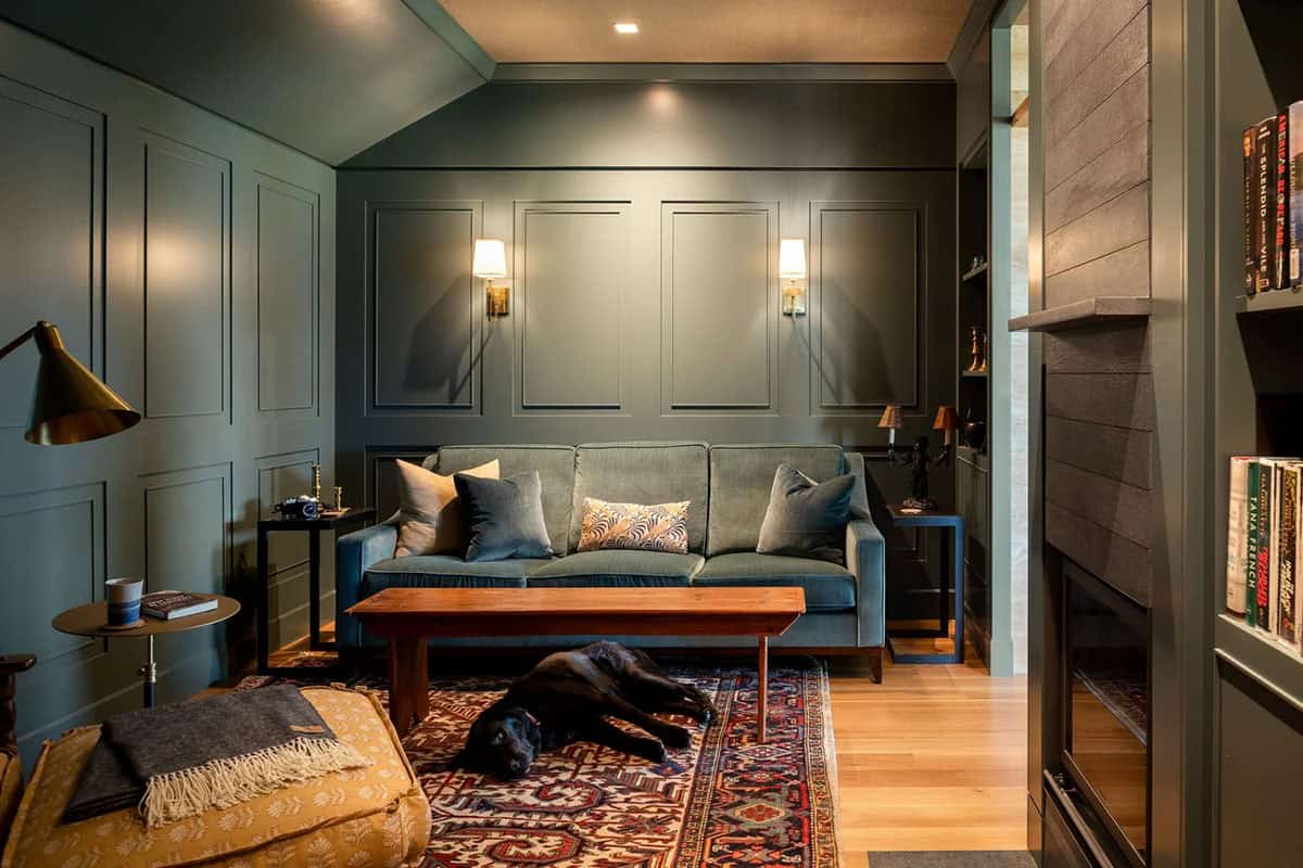 Cozy study with deep green paneled walls, velvet sofa, and built-in bookshelves beside a fireplace
