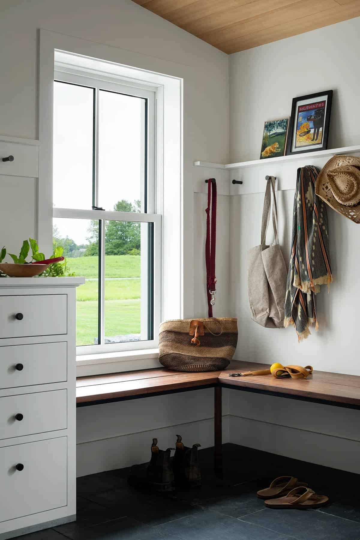 Mudroom with walnut bench, wall hooks, white drawers, and a window overlooking the lawn