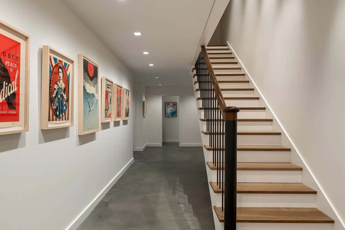 Lower-level hallway with framed art, polished concrete floor, and oak stair with steel balusters