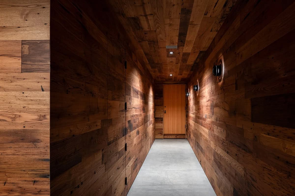 Lower-level hallway clad in reclaimed wood leading to a wood door