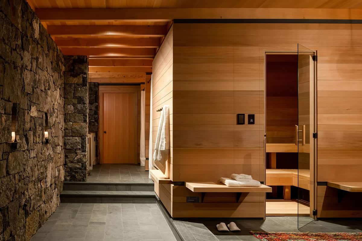 Below-grade spa entry with fieldstone wall, timber beam ceiling, cedar sauna, and slate floor