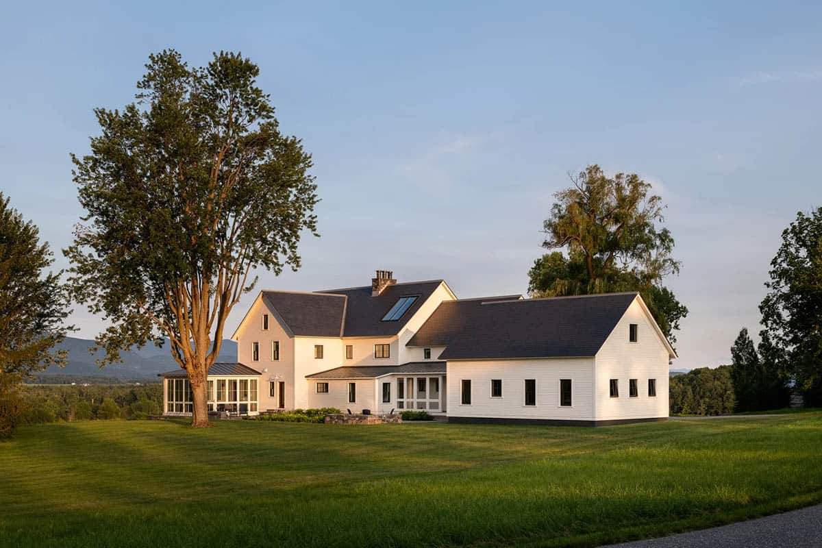 Rear of the modern farmhouse at golden hour with glass sunroom, slate roof, and skylight