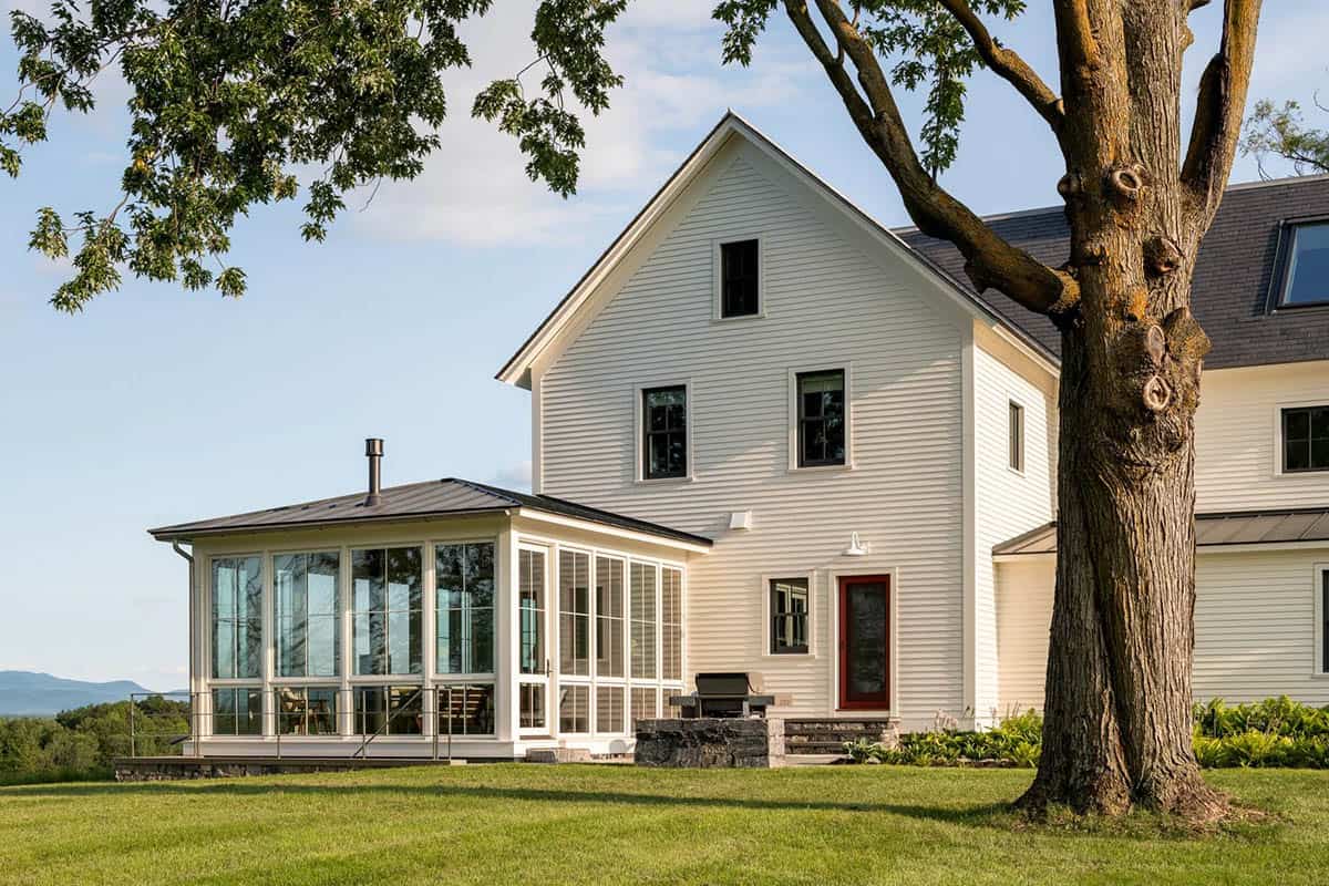 Glass sunroom with standing seam roof and red back door beside a stone grill surround