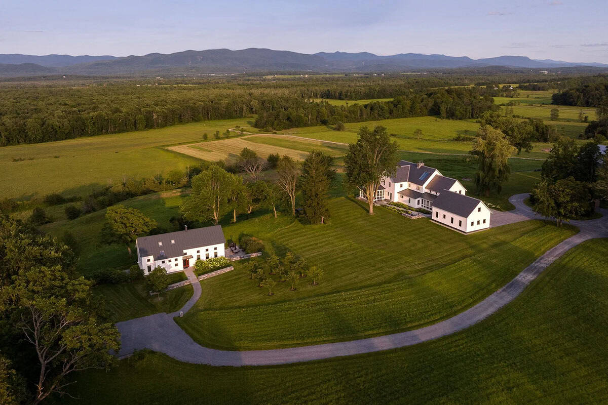 Aerial view of the farmhouse and second white building with a winding gravel drive through open fields