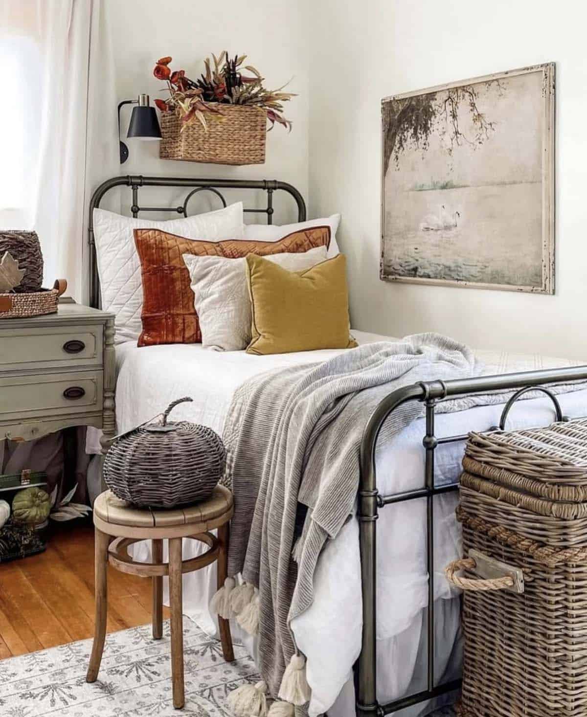 Iron bed with rust and mustard velvet pillows, gray tasseled throw, and woven pumpkin