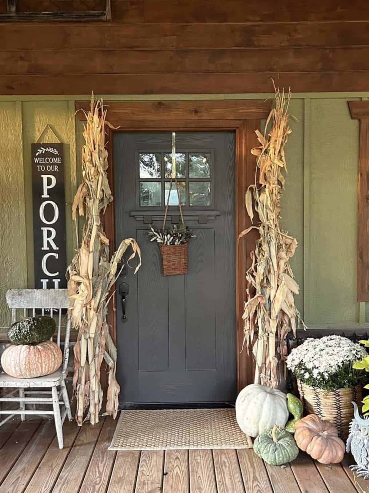Front porch with dried corn stalks, welcome sign, pumpkins, and white mums