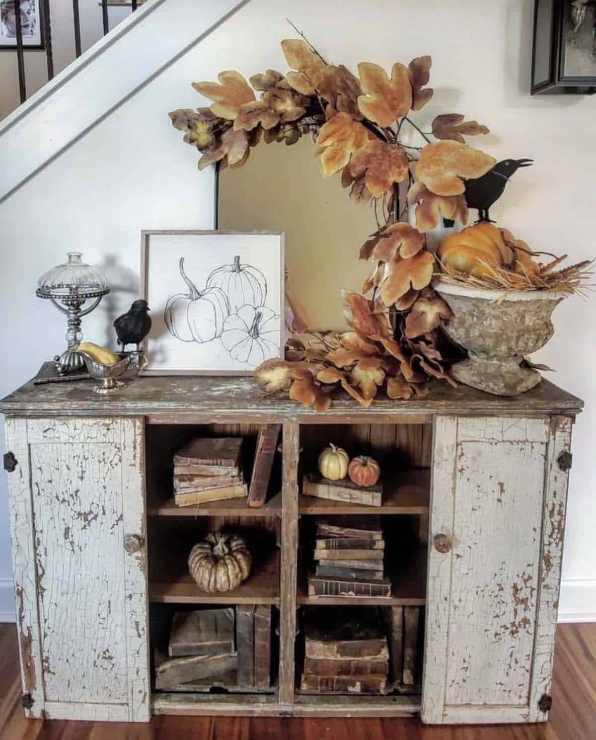 Entry table styled with fall leaf garland, mirror, pumpkins, and crow accents