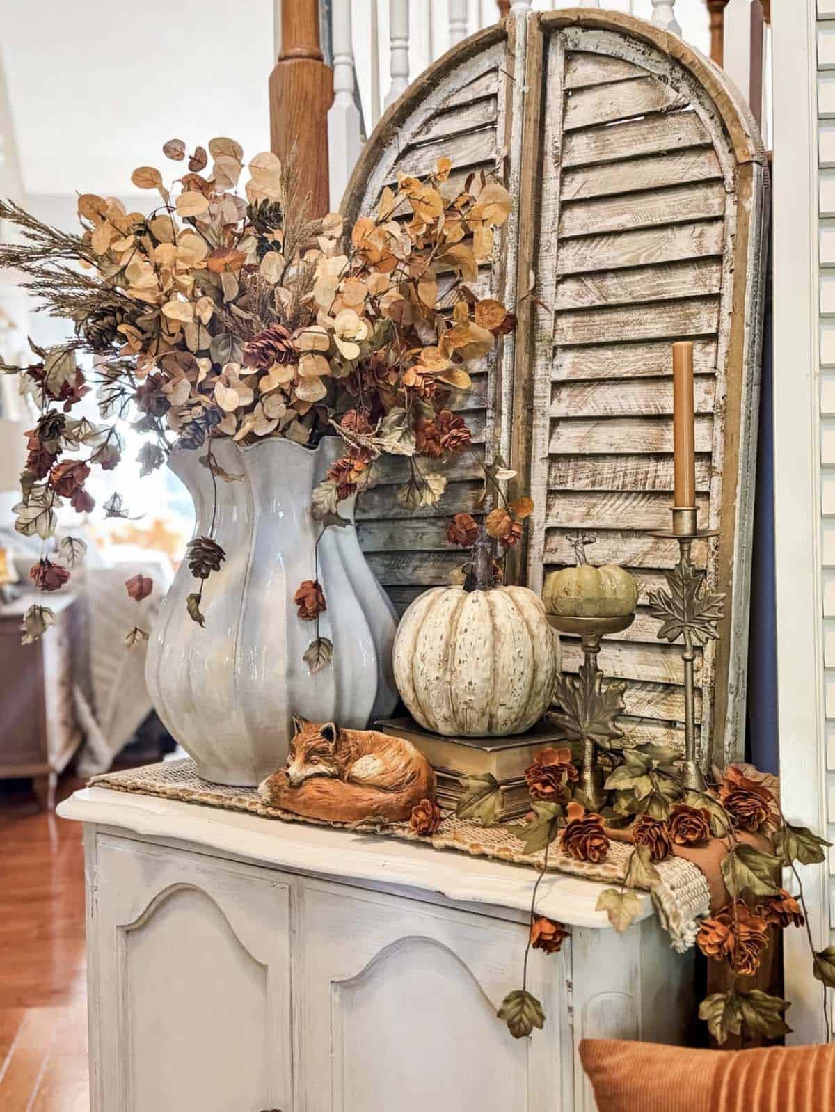 White cabinet with dried florals, pumpkin, fox figurine, and brass leaf candlestick