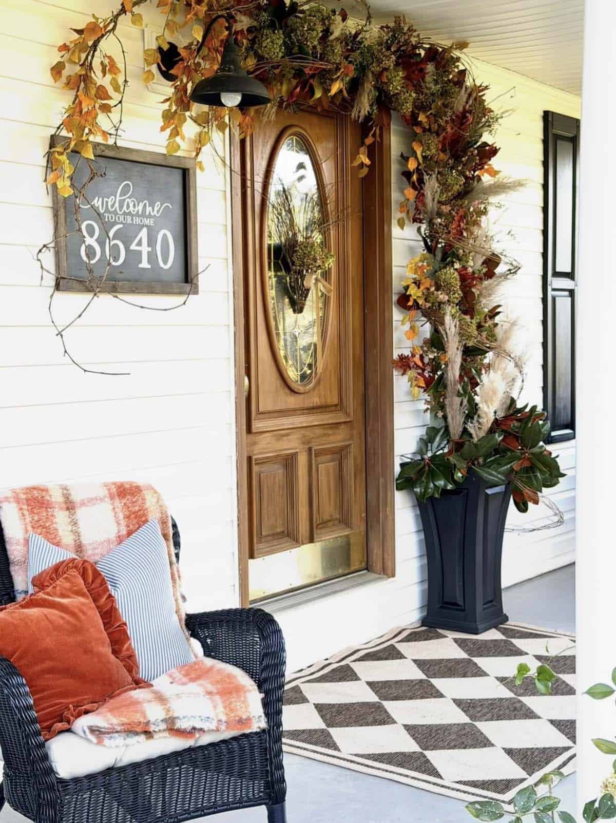 Wood front door with fall garland, magnolia planter, and wicker chair