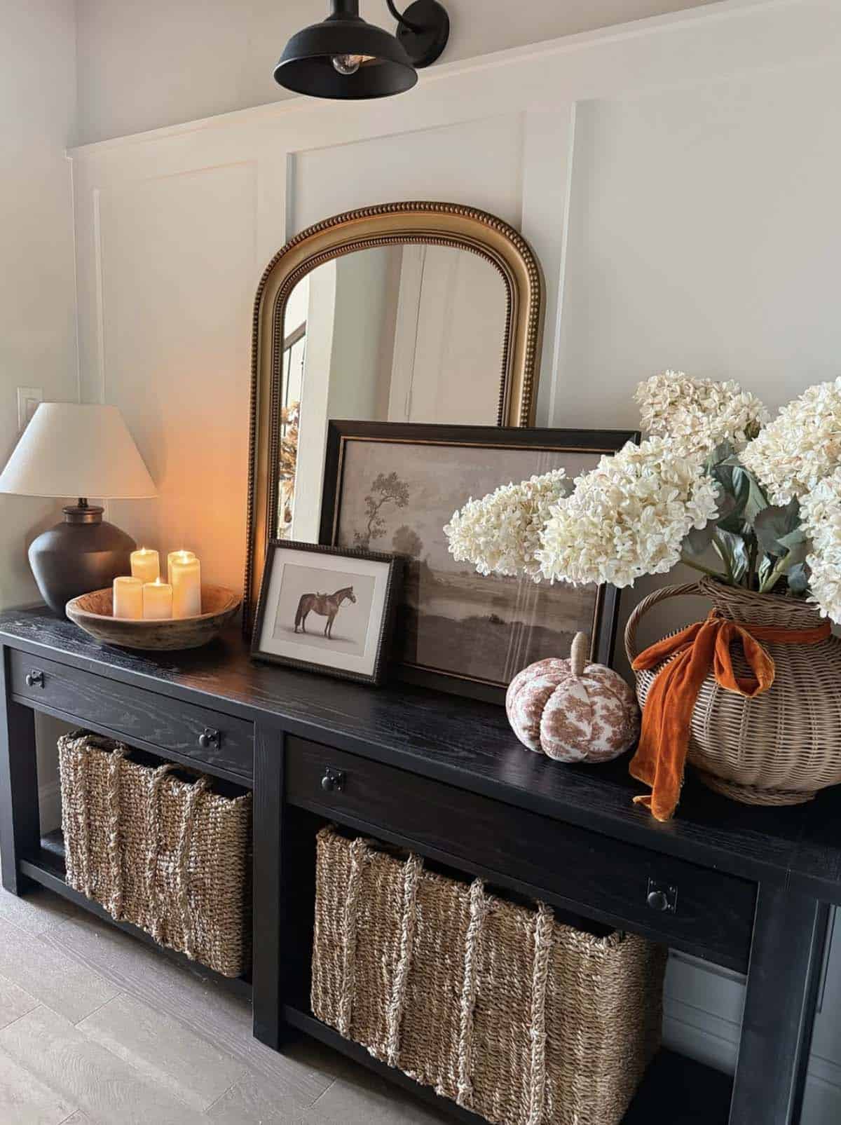 Black entry console with layered framed art, candles and a floral basket