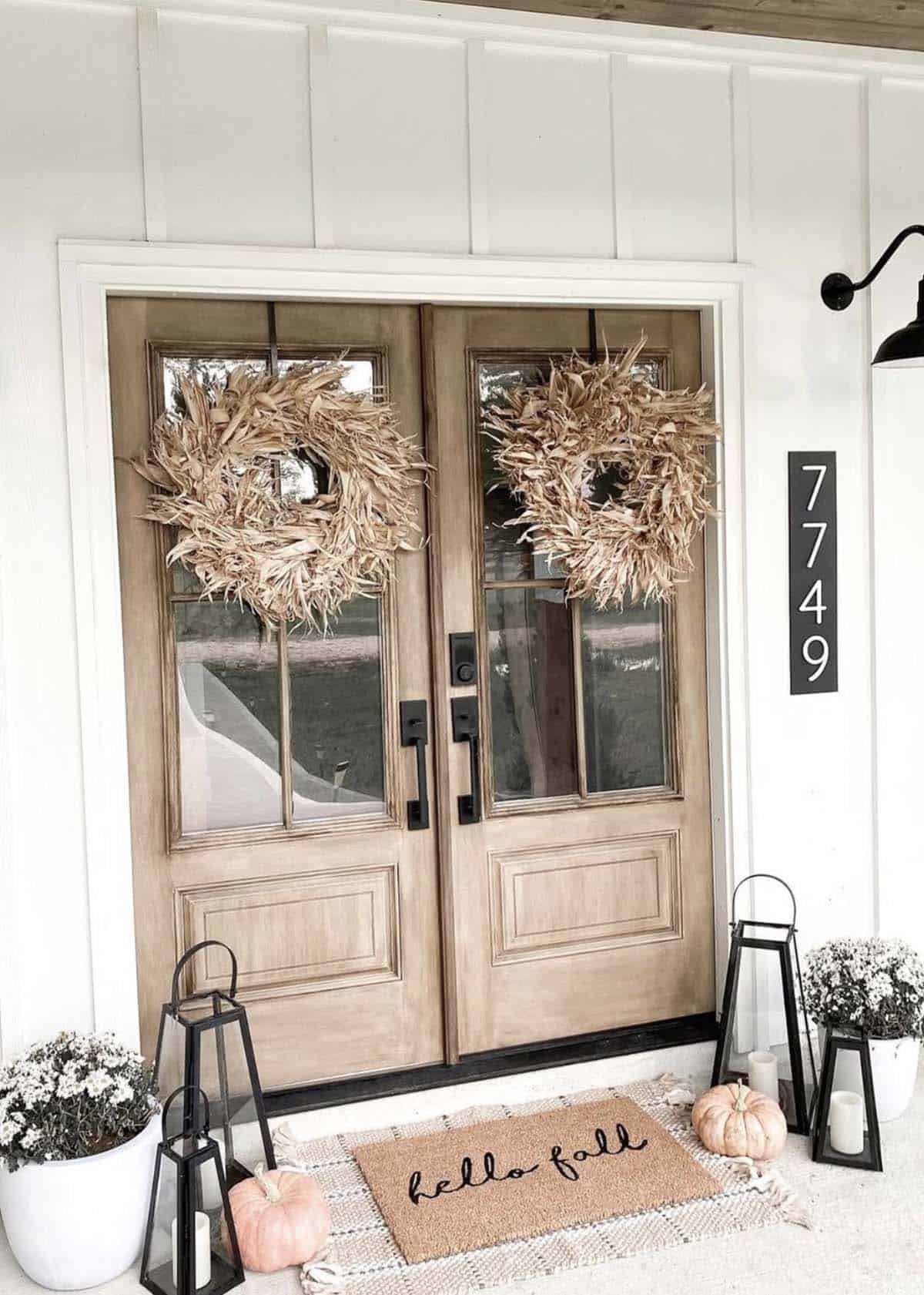Double wood front doors with dried wreaths, lanterns, and hello fall doormat