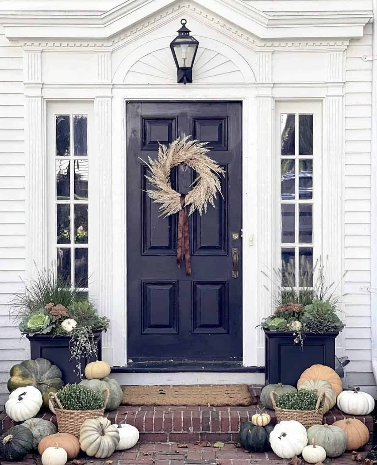 Black front door with fall planters, pumpkins, and dried grass wreath