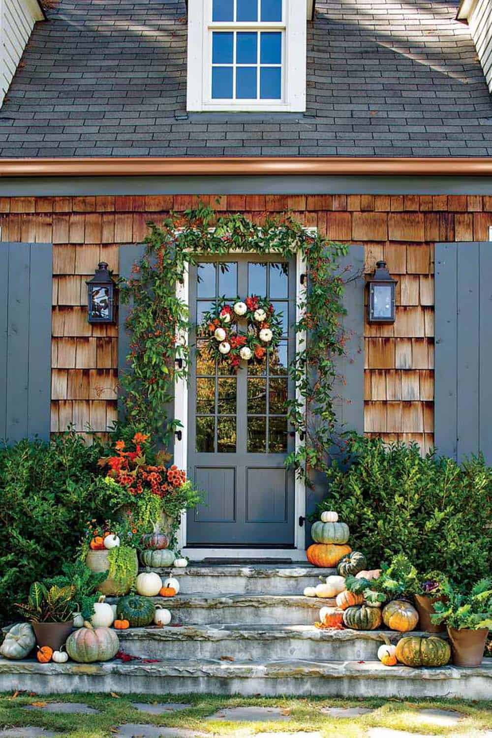 Gray front door with trailing greenery garland, mini pumpkin wreath, and stacked pumpkins on steps