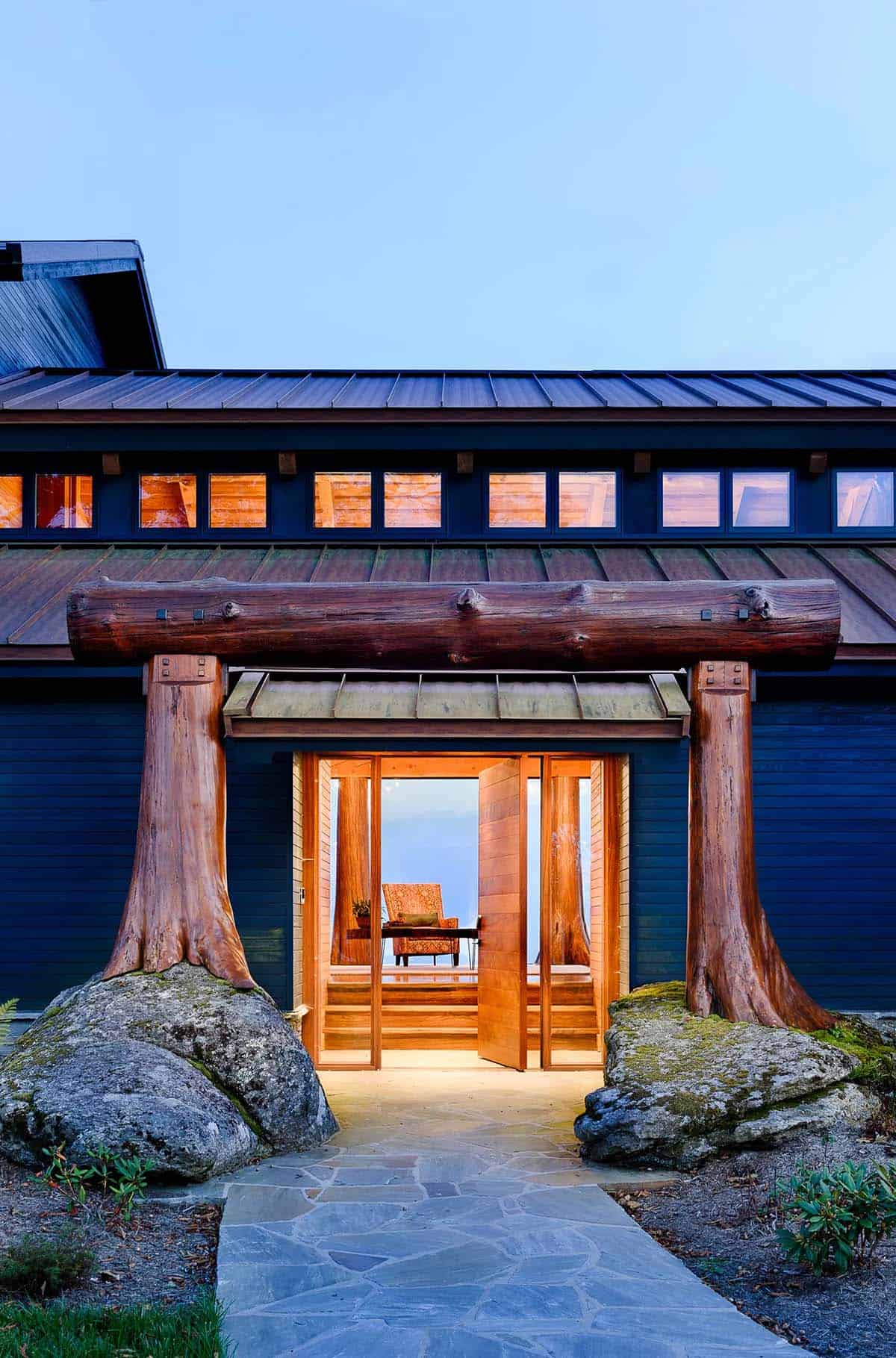 Timber portal entrance framed by tree trunk columns on boulders