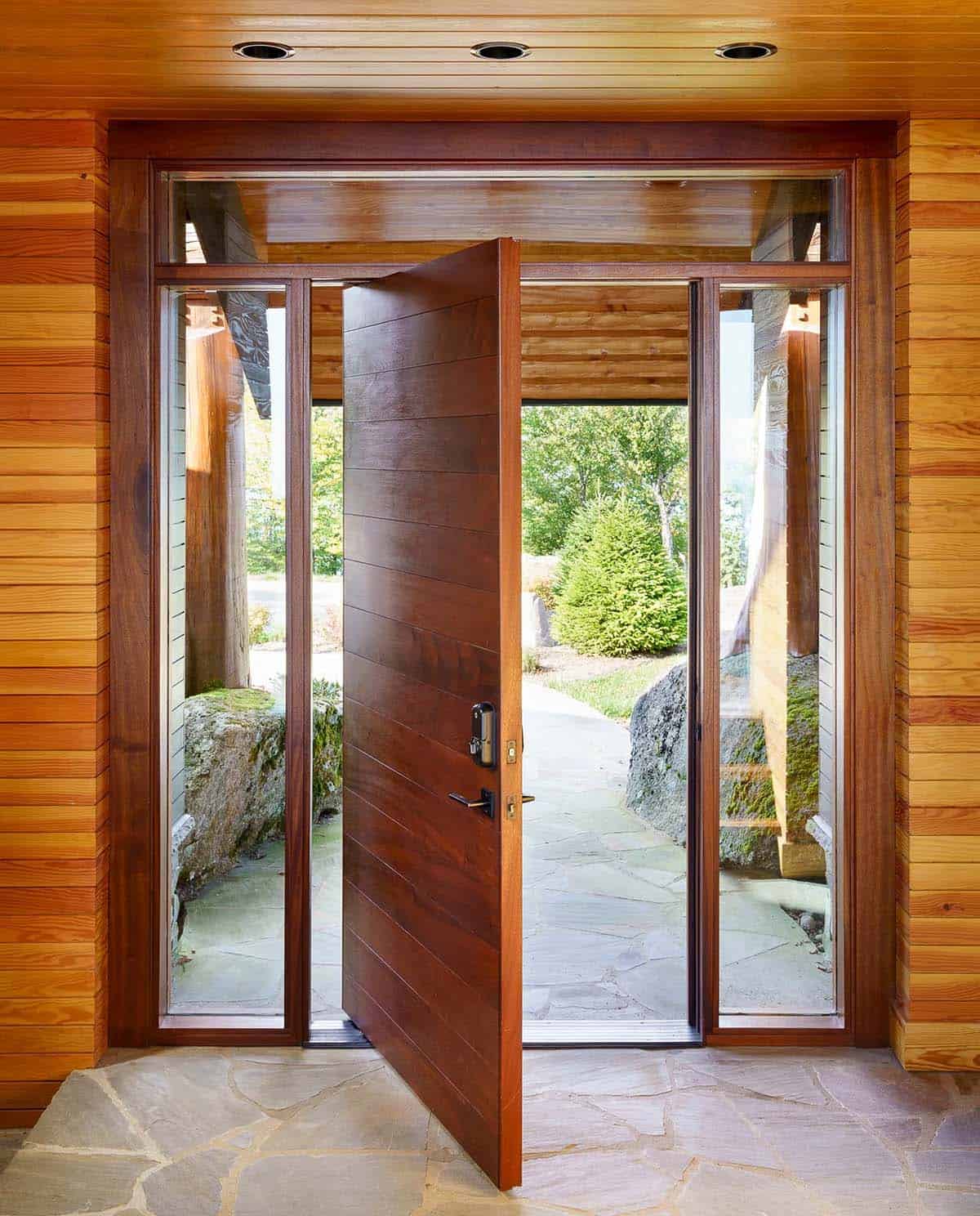 Wood pivot front door opens to a stone entry path