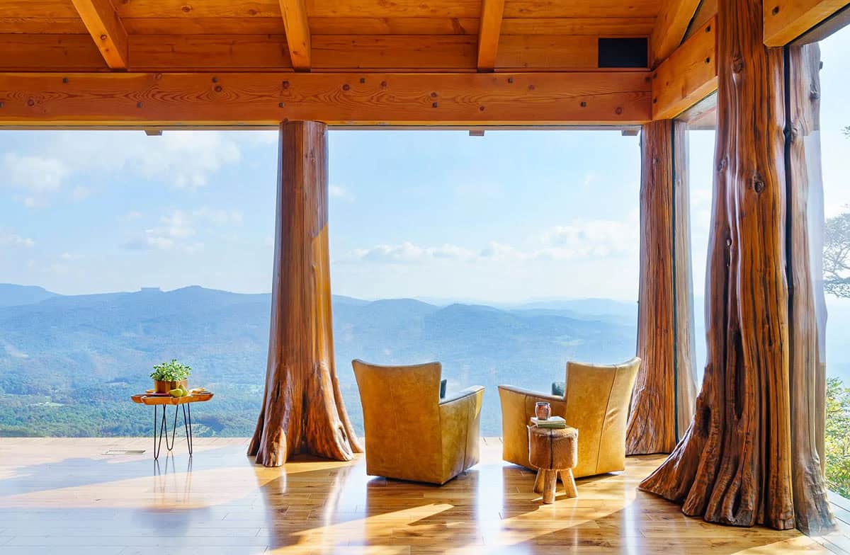 Two leather chairs sit between tree trunk columns facing mountain views