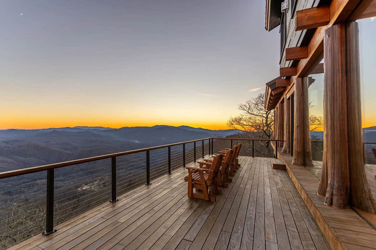 Wooden rocking chairs on a deck overlook mountains at sunset